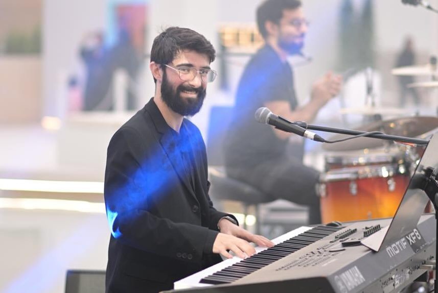 جورج أتناس مبتسمًا وهو يعزف على لوحة مفاتيح Yamaha خلال عرض حي، وخلفه عازف الدرامز.